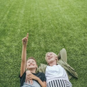 high angle view of happy mother and son looking up while lying together on green lawn